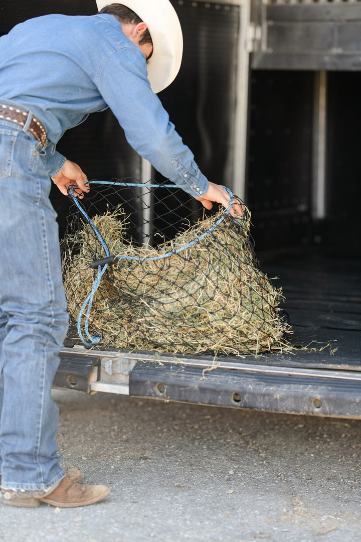 Cowboy bending over and filling a half bale hay net