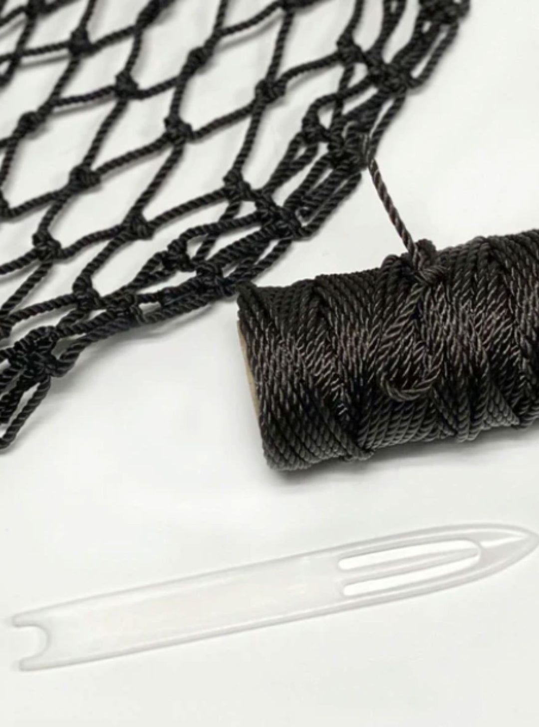 Hay Chix hay net repair kit featuring a spool of black twine, a plastic threading needle, and a section of black netting, designed for easy hay net repairs.